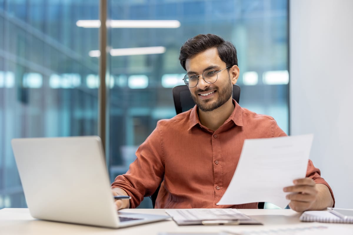 man using laptop while holding paperwork