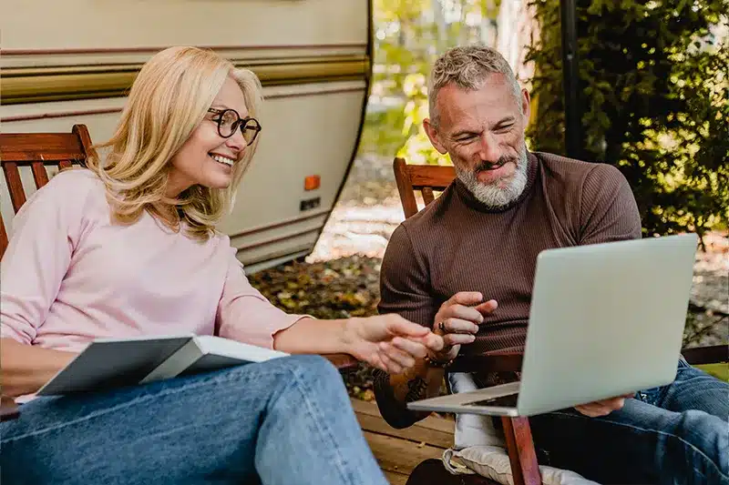 couple looking at laptop while sitting outside their camper