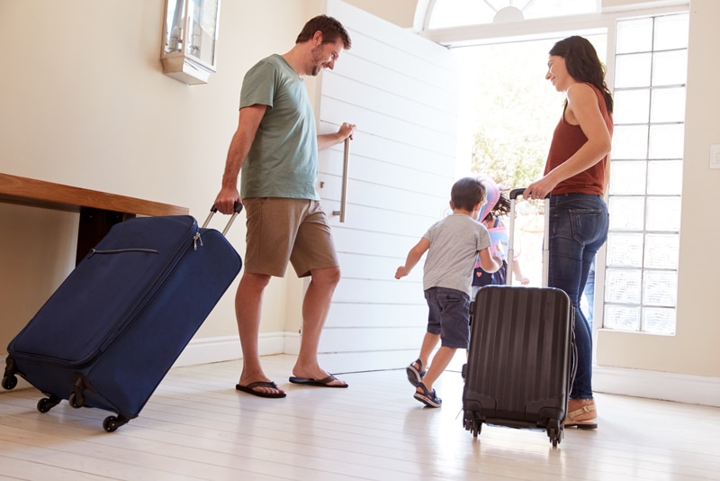 family leaving a home with travel cases