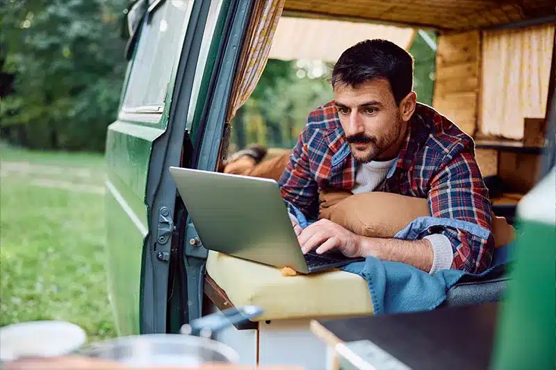 guy with mustache laying in camper van looking at laptop