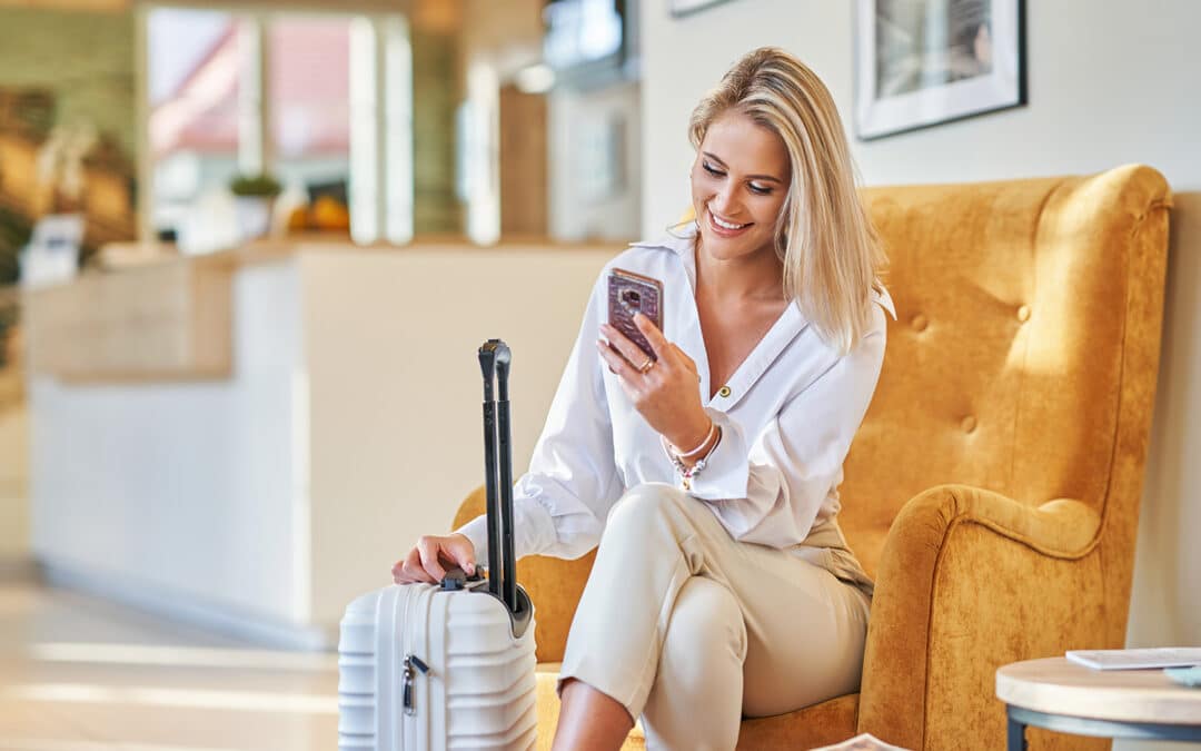 businesswoman with luggage in modern hotel lobby using smartphone